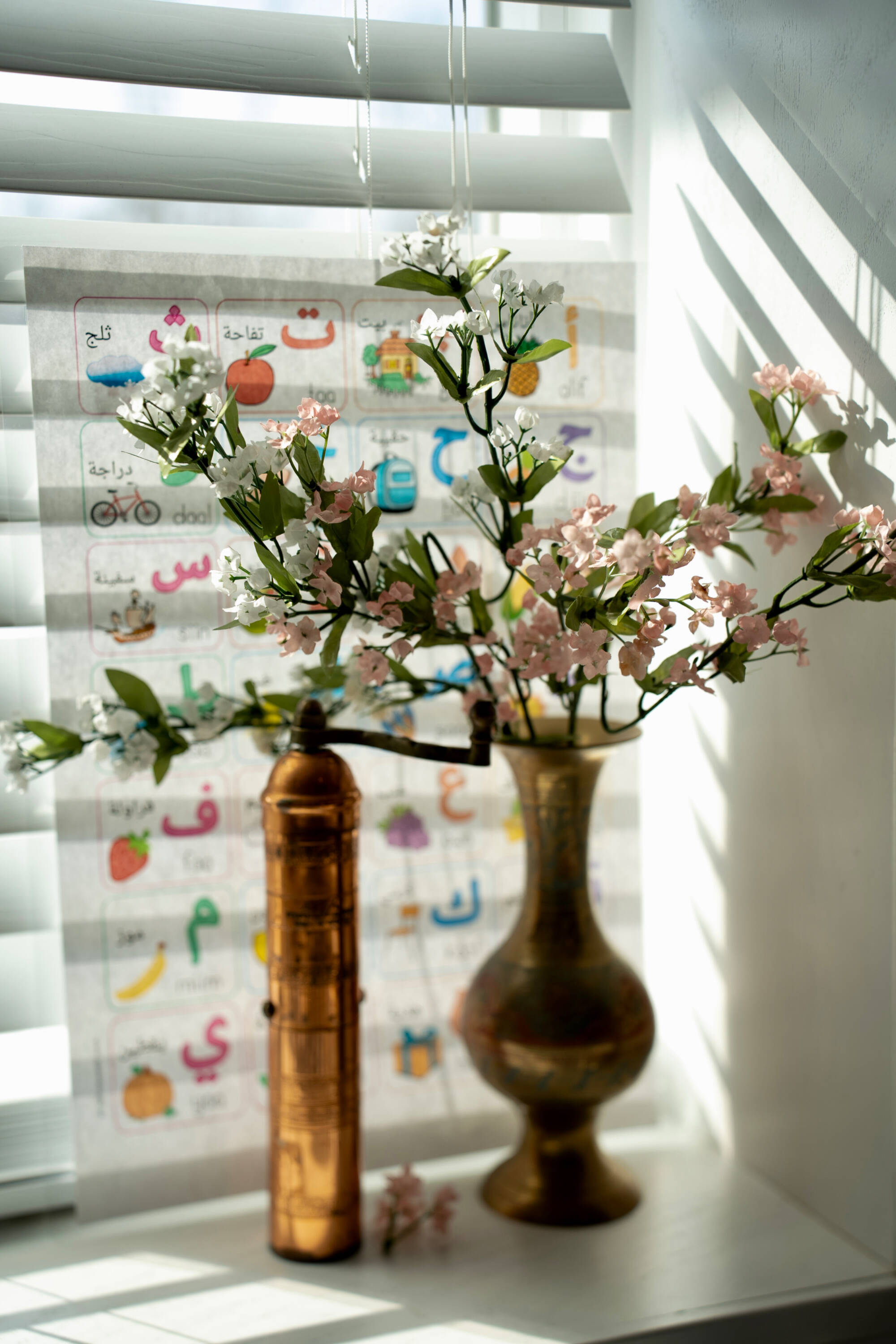 Flowers in a vase on a windowsill with a worksheet with the Arabic alphabet in the background.